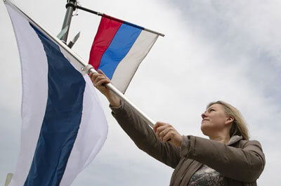 Kate Rybak flys an alternate Russian flag, used by anti-Putin organizers, underneath the Russian flag at 20th and Benjamin Franklin Parkway in Philadelphia on Thursday, April 21, 2022. (HEATHER KHALIFA / Philadelphia Inquirer)